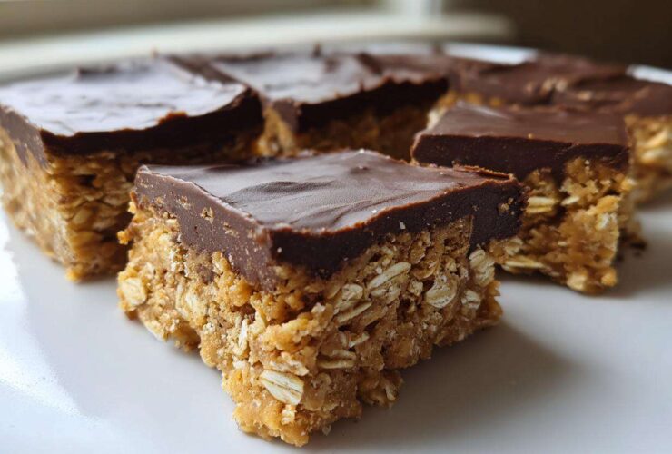 Close-up of several squares of No-Bake Chocolate Peanut Butter Oat Bars stacked on a white plate.