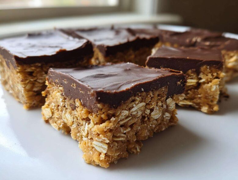 Close-up of several squares of No-Bake Chocolate Peanut Butter Oat Bars stacked on a white plate.