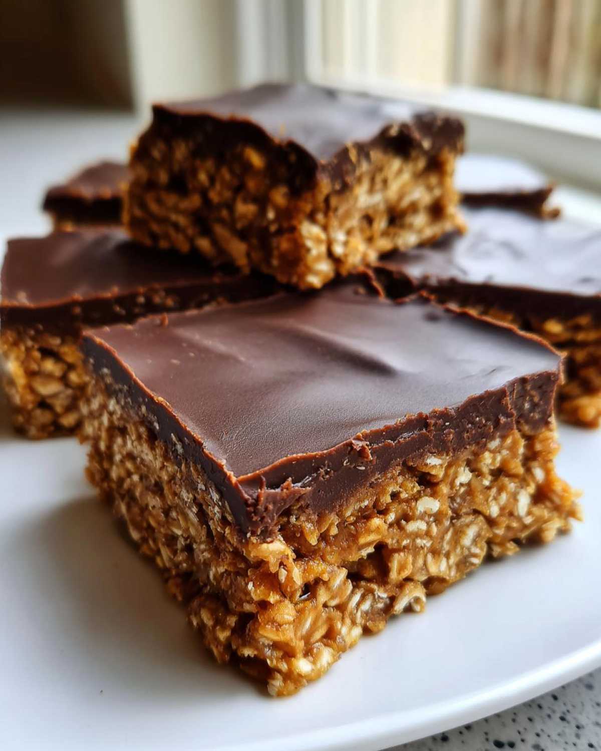 Close-up of rich No-Bake Chocolate Peanut Butter Oat Bars stacked on a white plate.