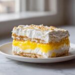 A perfect square slice of No-Bake Lemon Icebox Cake showing layers of graham crackers, bright yellow lemon filling, and whipped cream.