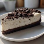 A thick slice of No-Bake Oreo Cheesecake with a creamy white filling and dark chocolate crust, topped with crushed Oreos.