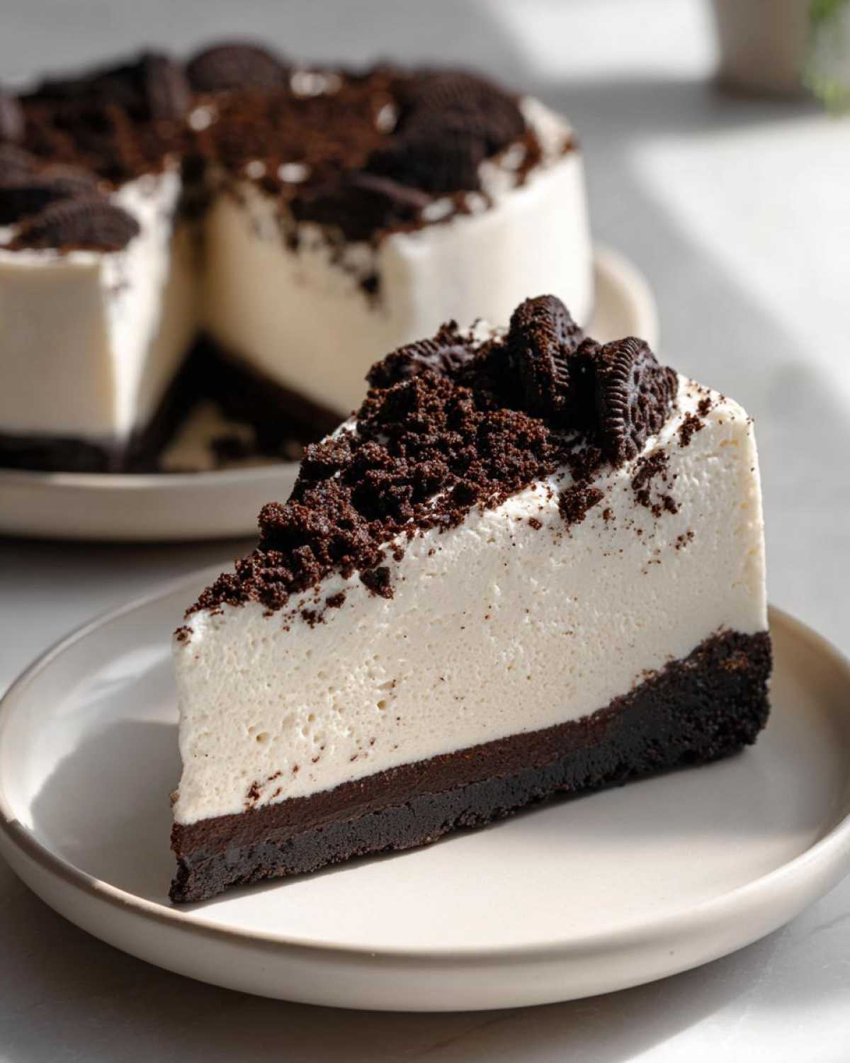 A perfect slice of No-Bake Oreo Cheesecake with a thick Oreo crust and creamy white filling, topped with crumbs and cookies.