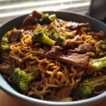 Close-up of One-Pot Beef and Broccoli Ramen Noodles coated in sauce, served in a blue bowl.