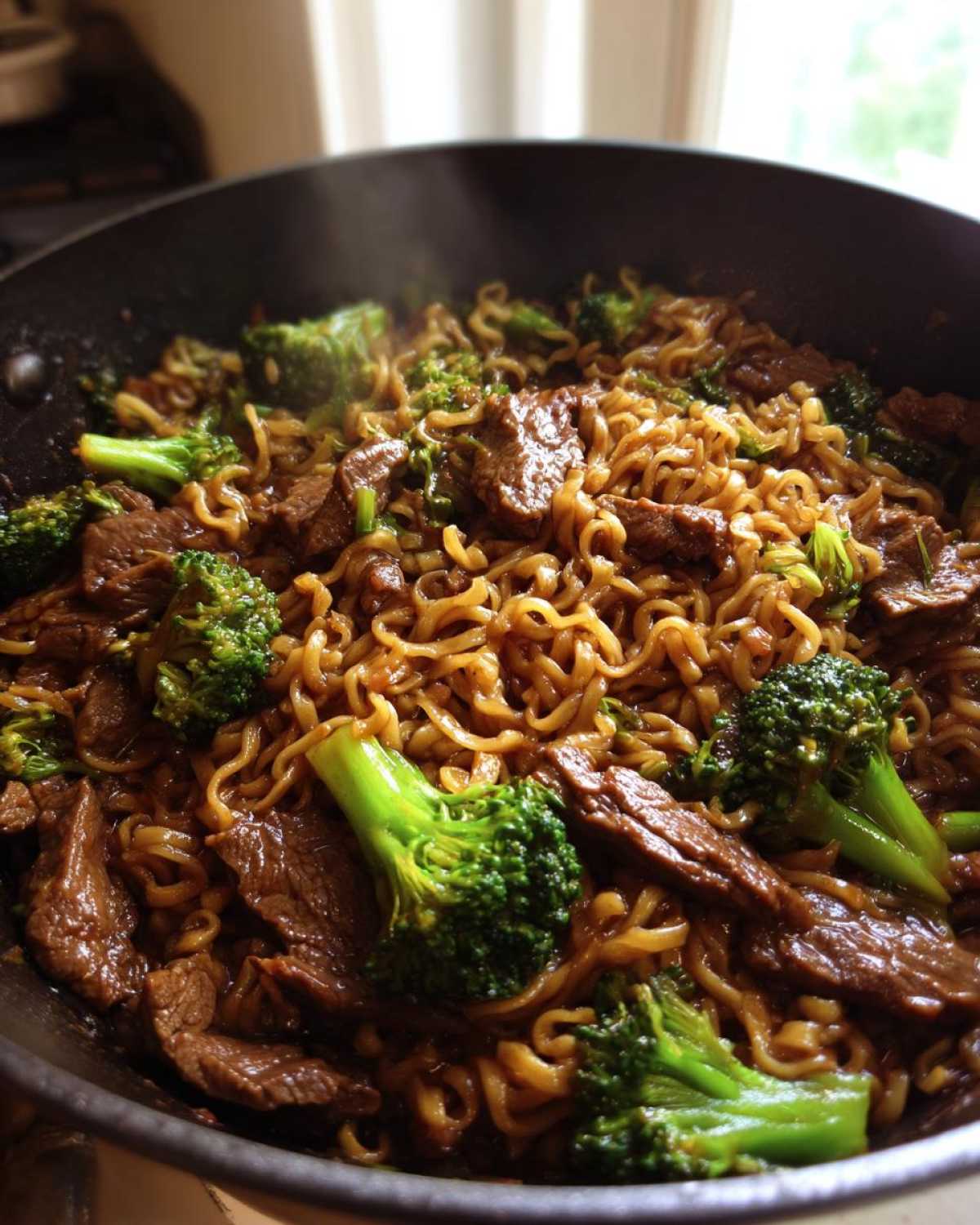 Close-up of steaming One-Pot Beef and Broccoli Ramen Noodles cooking in a dark skillet.