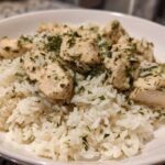 A close-up of cooked white rice topped with chunks of chicken breast seasoned with lemon and herbs.