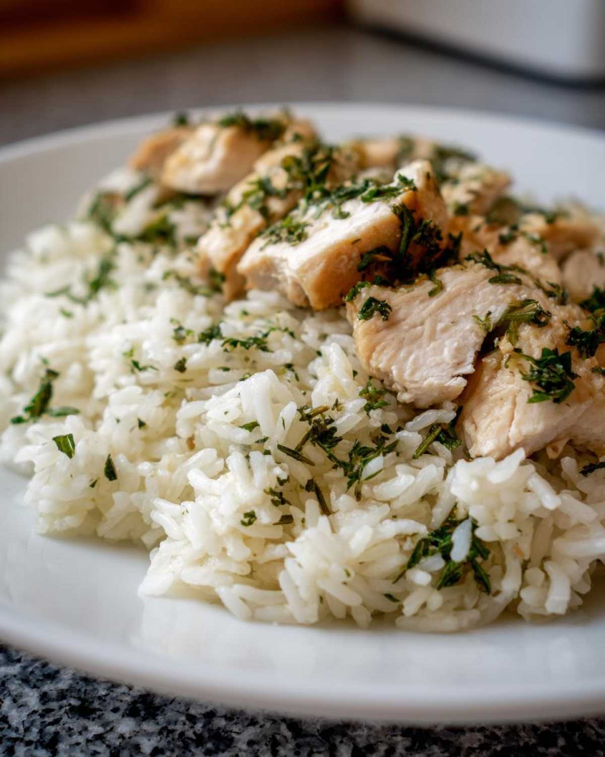 Close-up of cooked white rice topped with sliced chicken breast, seasoned with fresh herbs for One-Pot Chicken and Rice with Lemon and Herbs.