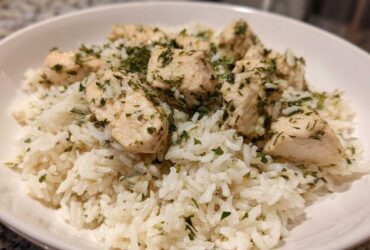 A close-up of cooked white rice topped with chunks of chicken breast seasoned with lemon and herbs.