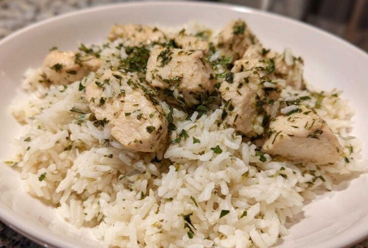A close-up of cooked white rice topped with chunks of chicken breast seasoned with lemon and herbs.