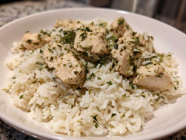 A close-up of cooked white rice topped with chunks of chicken breast seasoned with lemon and herbs.