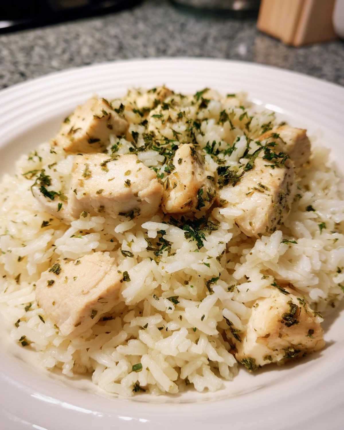 Close-up of fluffy white rice topped with cubed chicken breast and sprinkled generously with green herbs in a white bowl.
