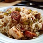 Close-up of a white bowl filled with One-Pot Chicken Jambalaya, featuring rice, chicken pieces, and sliced andouille sausage.