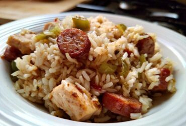 Close-up of a white bowl filled with One-Pot Chicken Jambalaya, featuring rice, chicken pieces, and sliced andouille sausage.