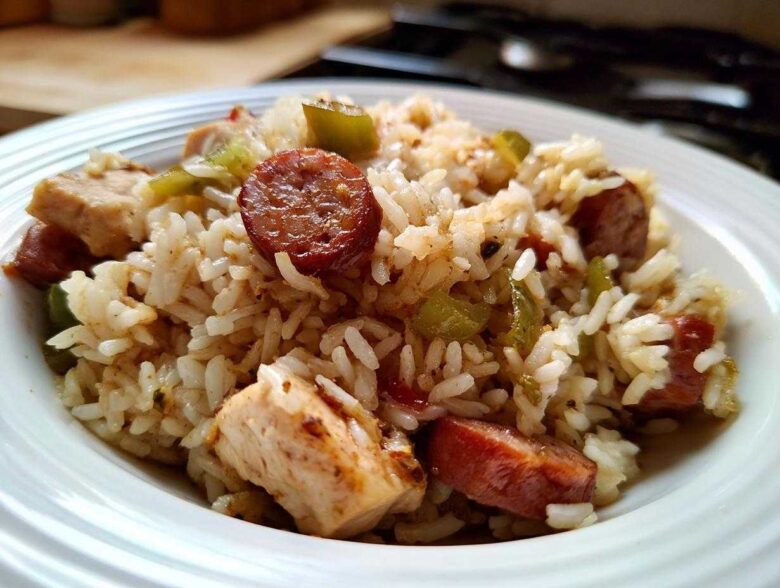 Close-up of a white bowl filled with One-Pot Chicken Jambalaya, featuring rice, chicken pieces, and sliced andouille sausage.