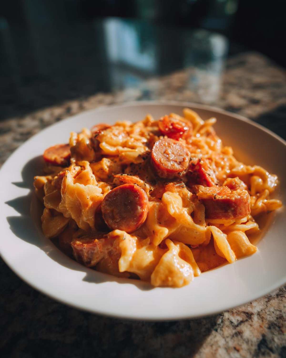 A close-up of a white bowl filled with One-Pot Creamy Cajun Sausage Pasta, topped with sliced sausage.