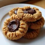 A stack of freshly baked Peanut Butter Blossom Cookies featuring a rich chocolate center on a white plate.