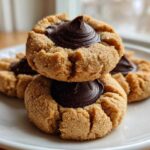 Close-up of stacked Peanut Butter Blossom Cookies with a rich chocolate kiss center on a white plate.