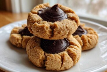Close-up of stacked Peanut Butter Blossom Cookies with a rich chocolate kiss center on a white plate.