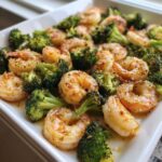 Close-up of juicy shrimp and bright green broccoli florets coated in garlic butter sauce.