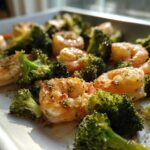 Close-up of cooked shrimp and broccoli florets seasoned with garlic butter on a white sheet pan.