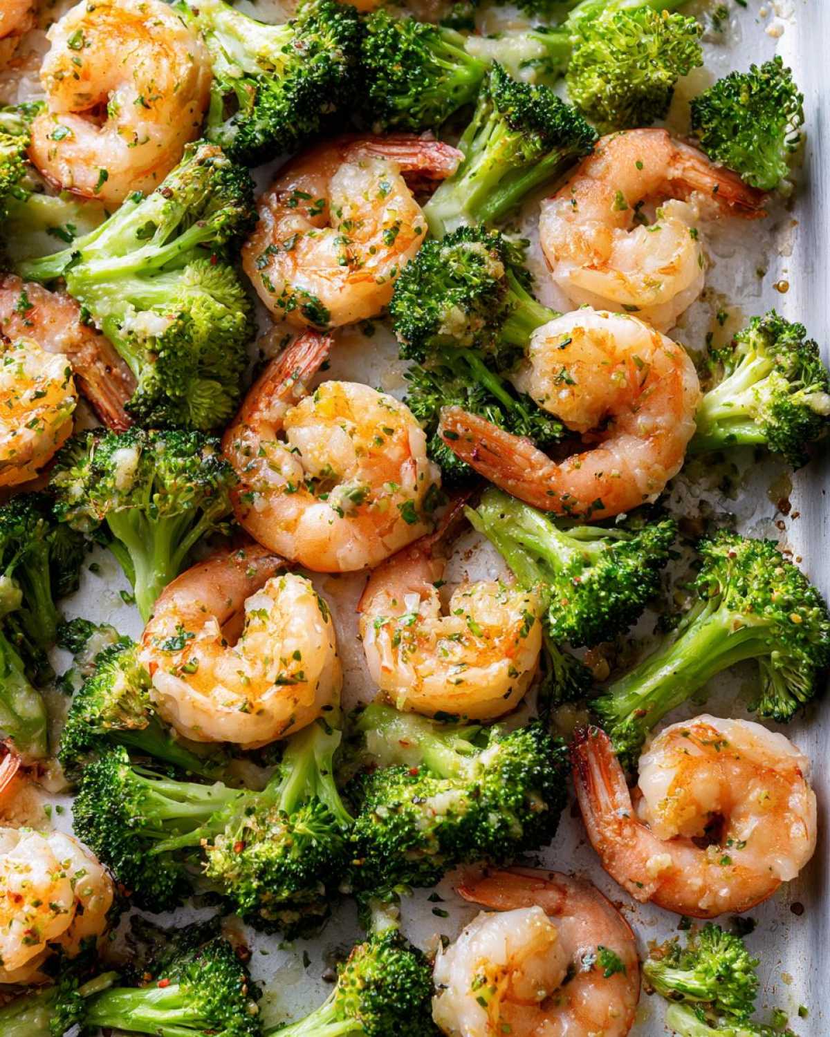 Close-up of cooked shrimp and bright green broccoli florets seasoned with garlic butter on a sheet pan.