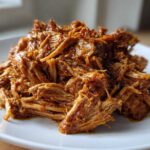 A close-up of tender, shredded Slow Cooker Honey Garlic Pulled Pork piled high on a white plate.
