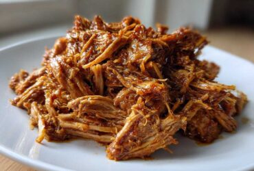 A close-up of tender, shredded Slow Cooker Honey Garlic Pulled Pork piled high on a white plate.