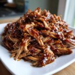 A close-up of shredded, saucy Slow Cooker Honey Garlic Pulled Pork piled high on a white plate.