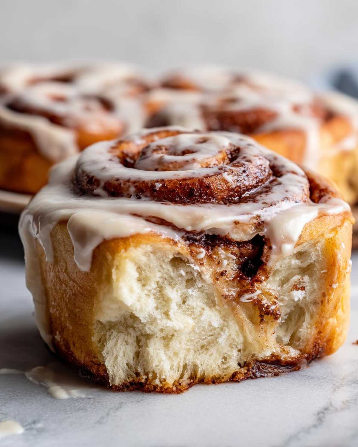 Close-up of a soft Gluten-Free Cinnamon Roll with a bite taken out, showing the fluffy interior and cream cheese icing.
