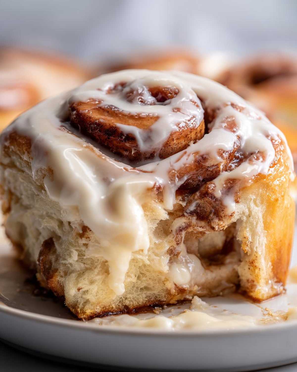 Close-up of a soft Gluten-Free Cinnamon Roll covered in thick, dripping cream cheese icing.