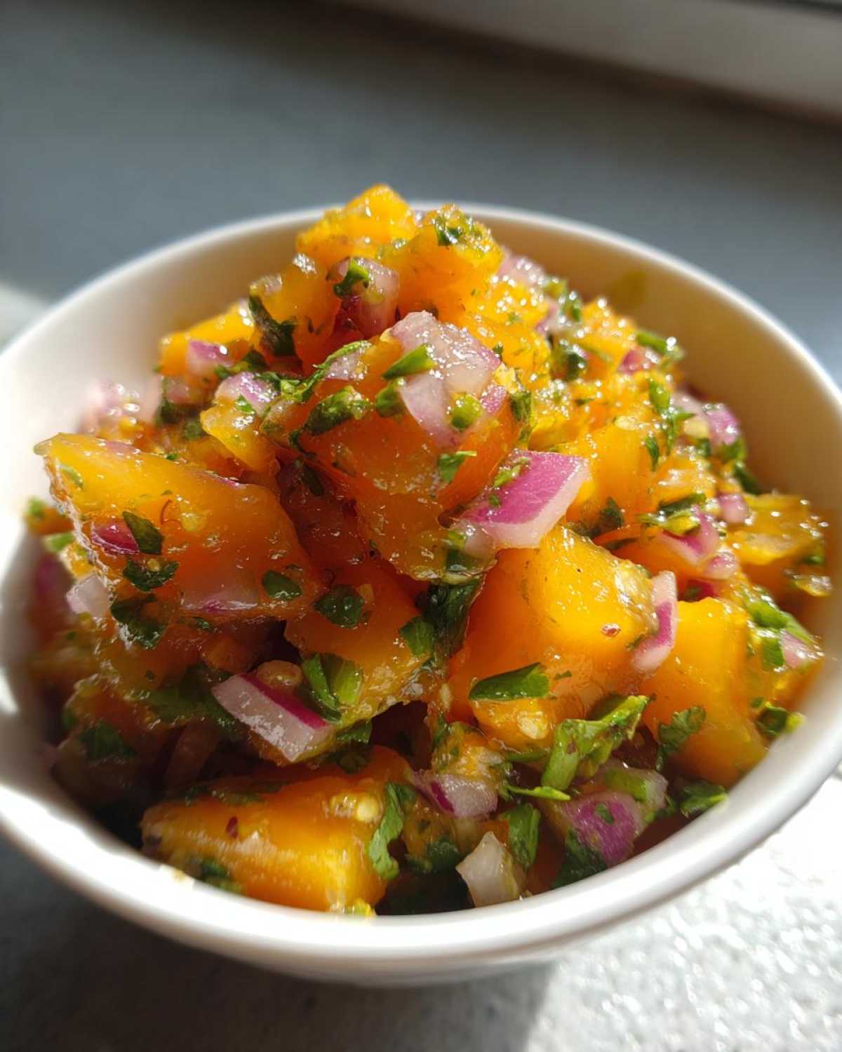 Close-up of bright orange mango chunks mixed with red onion and cilantro in a white bowl, showcasing the Spicy Mango Salsa.