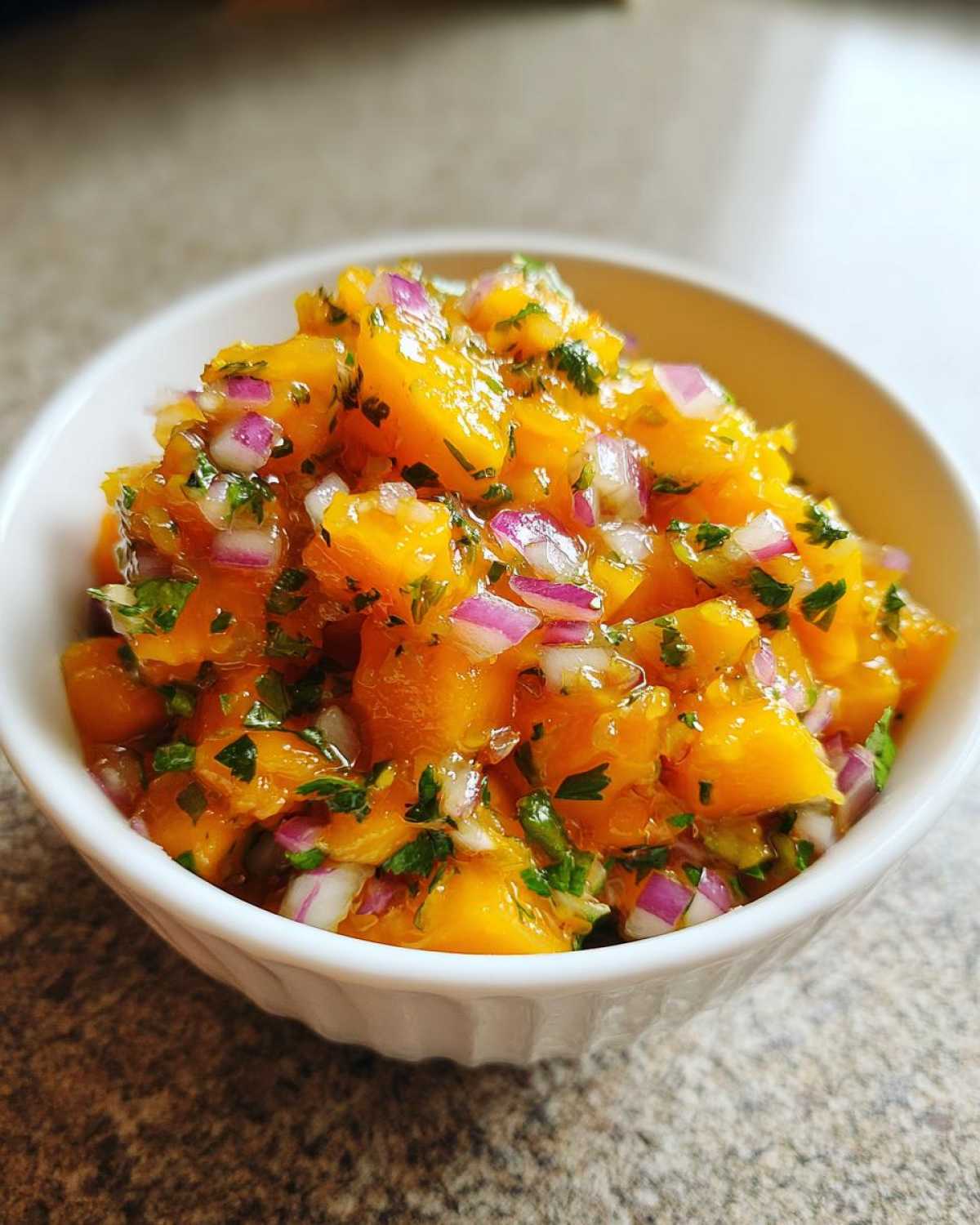 Close-up of bright orange Spicy Mango Salsa featuring diced mango, red onion, and cilantro in a small white bowl.