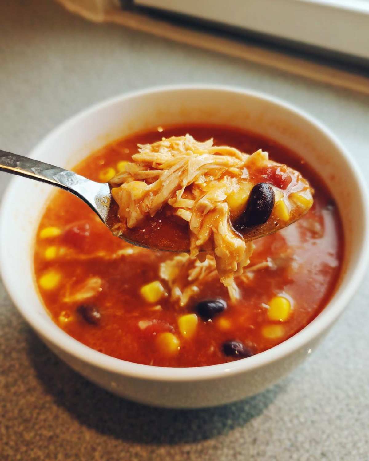 A spoonful of shredded chicken, black beans, and corn lifted from a bowl of vibrant Instant Pot Chicken Tortilla Soup.
