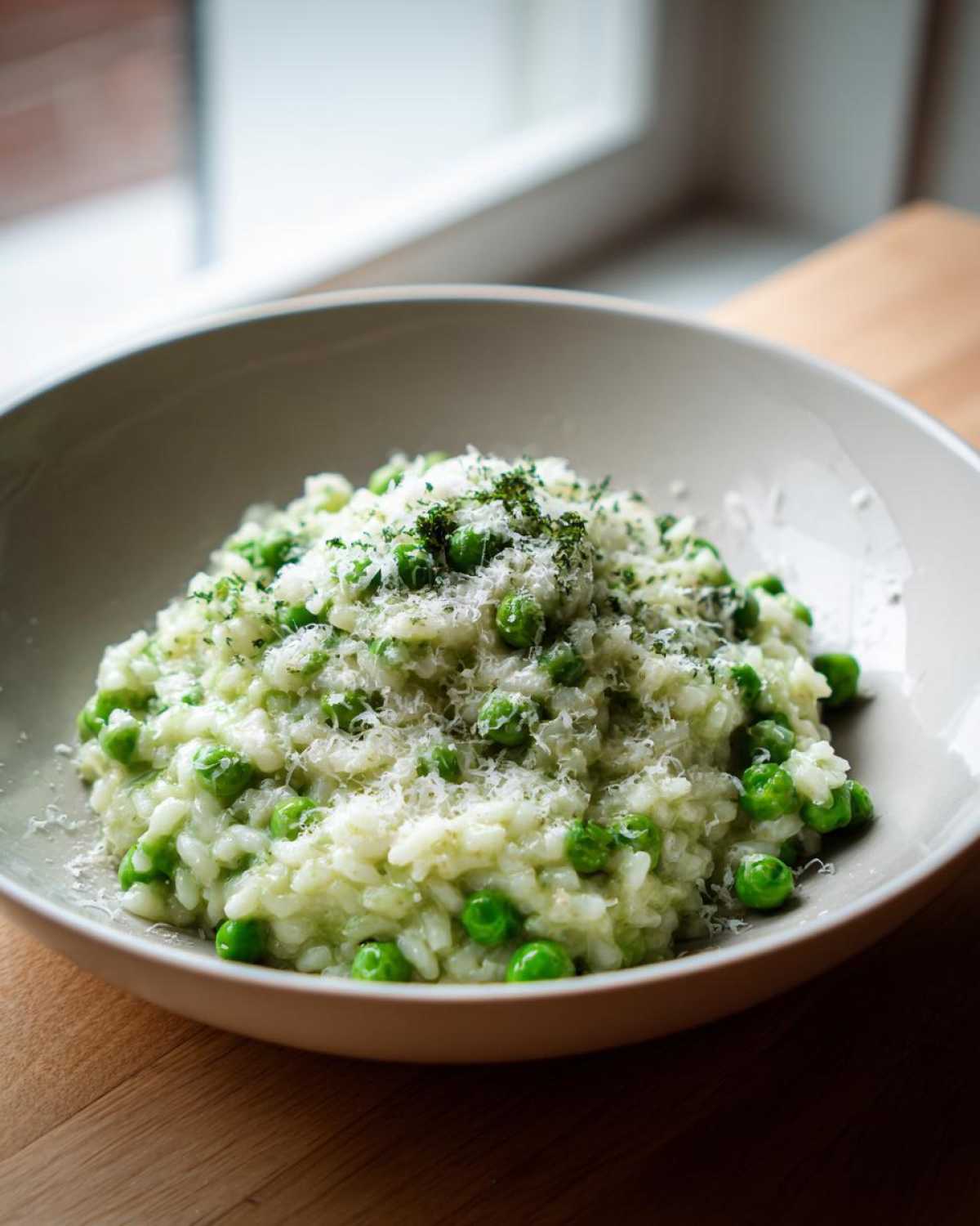 A close-up of creamy Spring Pea and Mint Risotto topped with grated Parmesan and herbs.