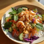A vibrant Spring Roll Bowl with Peanut Sauce featuring shrimp, rice noodles, cucumber, carrots, and fresh mint.
