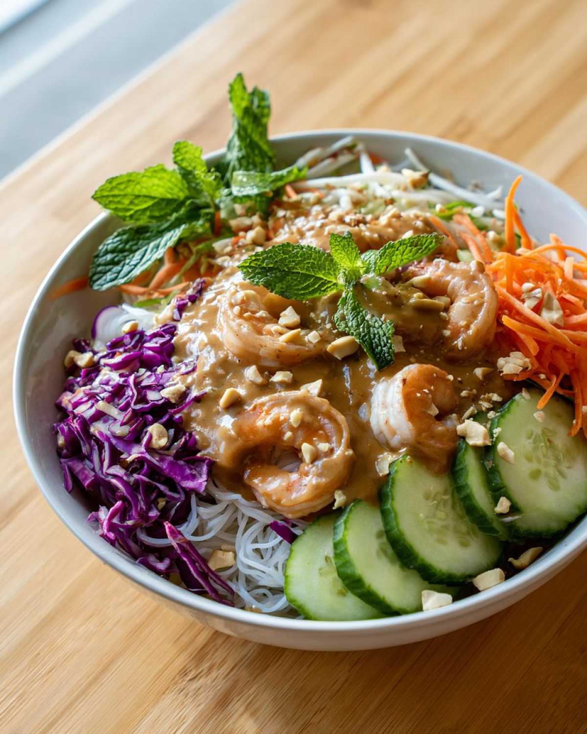 A vibrant Spring Roll Bowl with Peanut Sauce featuring shrimp, vermicelli noodles, cucumber, and mint.