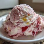 Close-up of two scoops of pink and white Strawberry Banana Ice Cream with visible fruit pieces in a small white bowl.