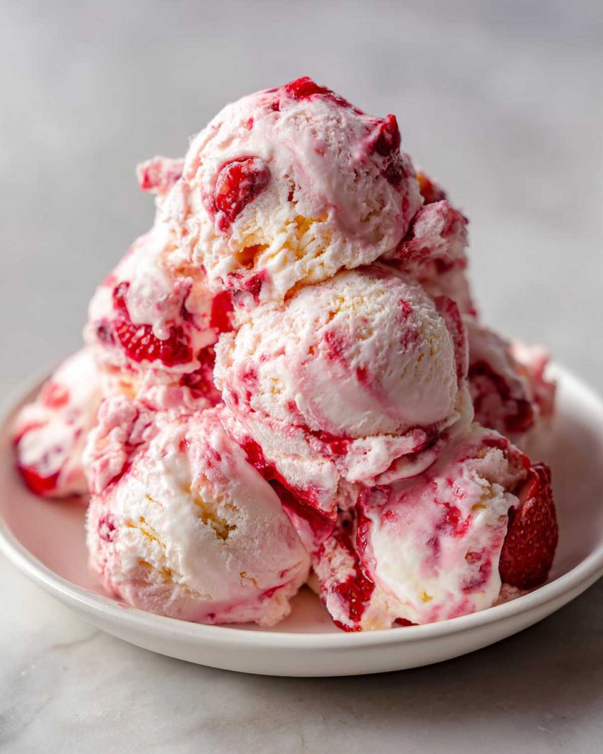 A mound of creamy Strawberry Banana Ice Cream scoops swirled with bright red strawberry pieces on a white plate.