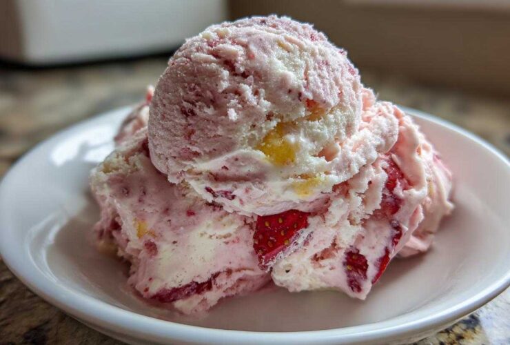 Close-up of two scoops of pink and white Strawberry Banana Ice Cream with visible fruit pieces in a small white bowl.