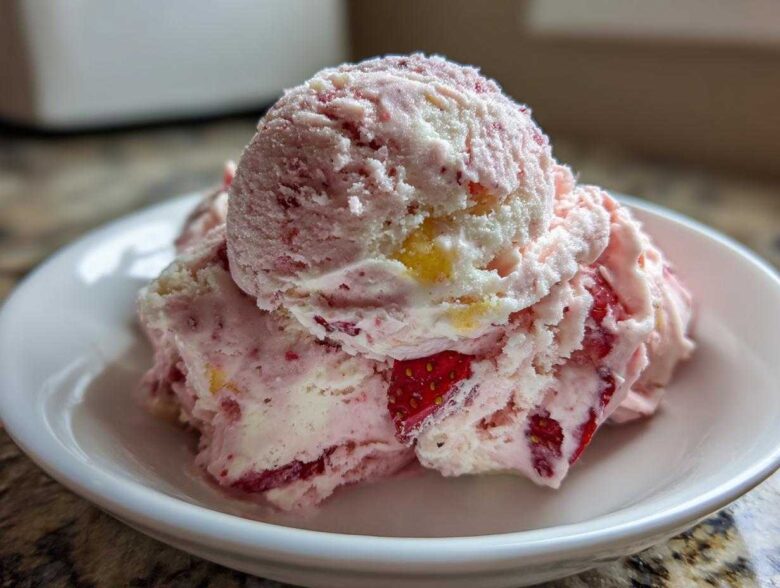 Close-up of two scoops of pink and white Strawberry Banana Ice Cream with visible fruit pieces in a small white bowl.