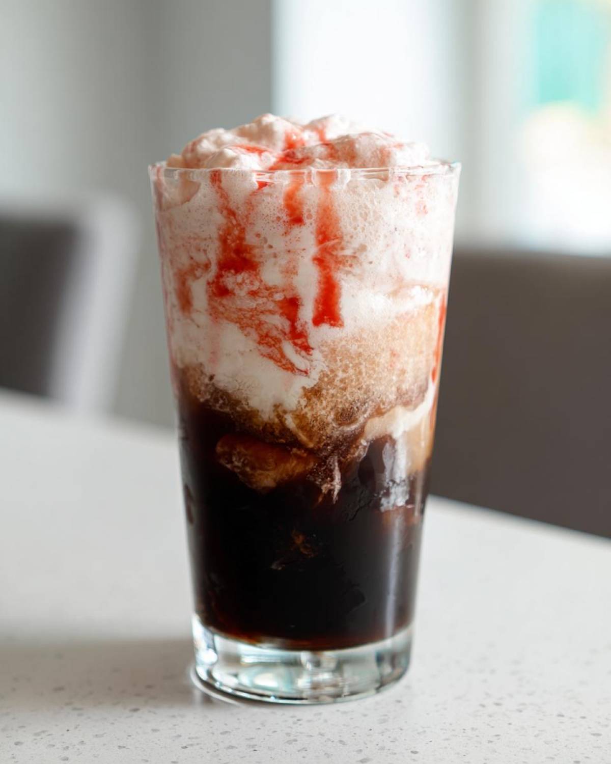 A tall glass showing the layers of Strawberry Cream Cold Brew, featuring dark coffee, foam, and strawberry drizzle.