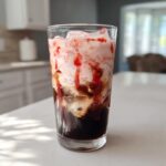 Close-up of a tall glass filled with Strawberry Cream Cold Brew, showing layers of dark coffee, pink cream, and strawberry syrup.