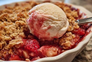Close-up of warm Strawberry Rhubarb Crisp topped with a melting scoop of vanilla ice cream.