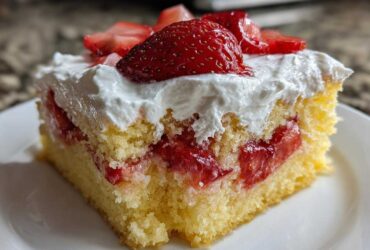 Close-up of a moist slice of Strawberry Shortcake Sheet Cake layered with strawberries and topped with whipped cream.