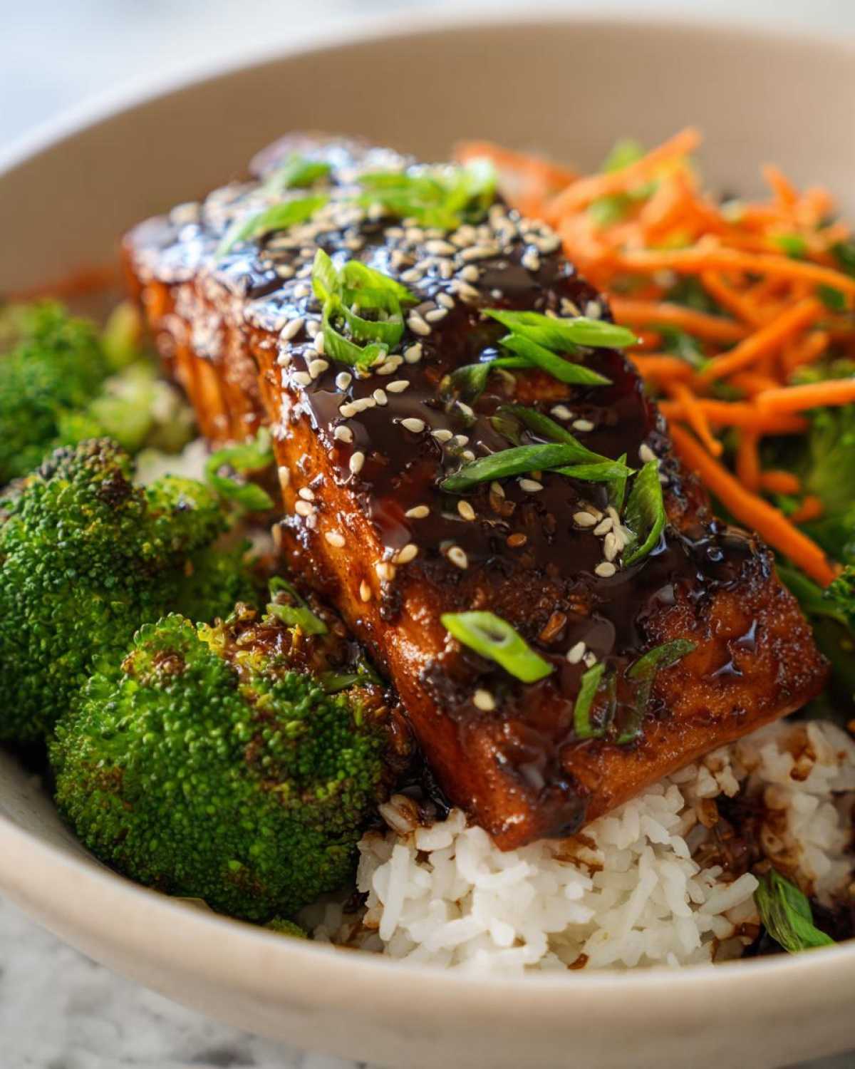 Close-up of a piece of glazed salmon topped with sesame seeds and green onions in a Teriyaki Salmon Rice Bowls.