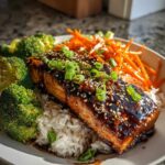 A close-up of a Teriyaki Salmon Rice Bowls featuring glazed salmon over rice with broccoli and shredded carrots.