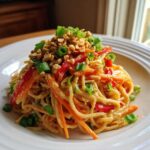 A close-up of a plate of Thai Peanut Noodles with Crunchy Veggies, topped with peanuts and scallions.