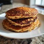 A tall stack of three perfectly golden-brown Vegan Banana Oat Pancakes served on a white plate.