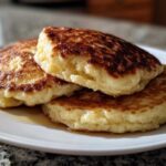 A close-up of three fluffy Vegan Banana Oat Pancakes stacked on a white plate with a drizzle of syrup.