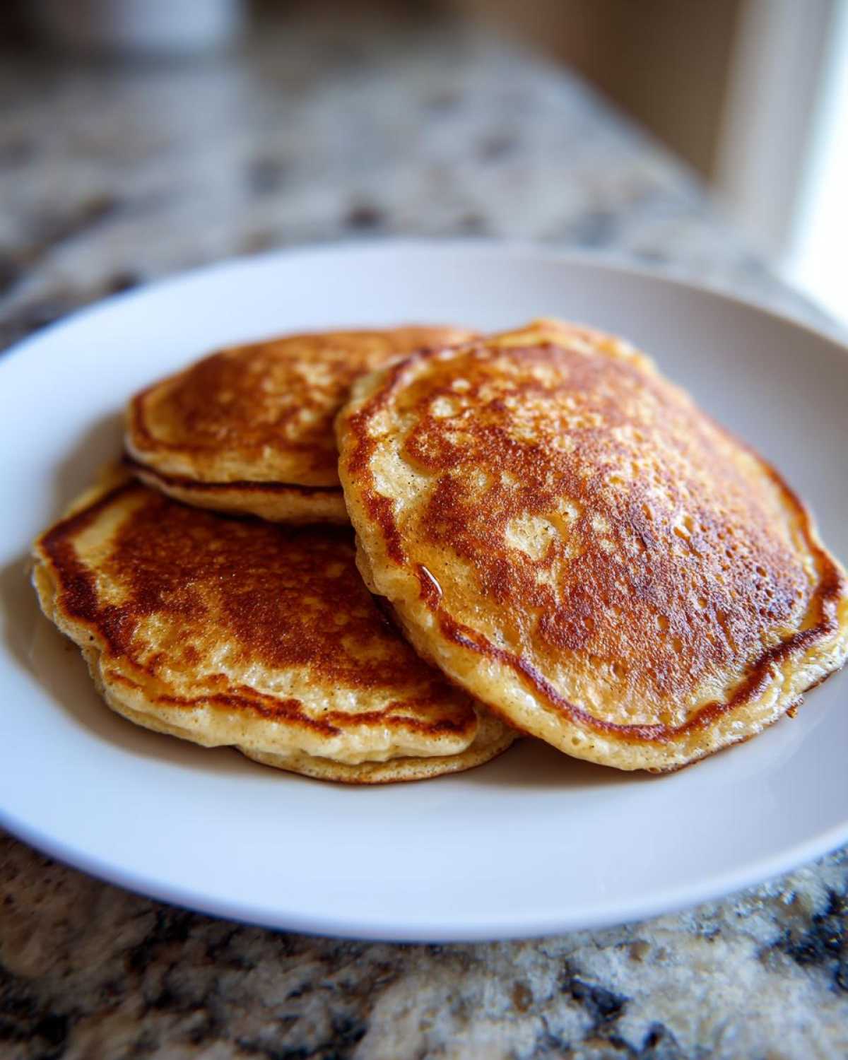 Close-up of three golden-brown Vegan Banana Oat Pancakes stacked on a white plate.