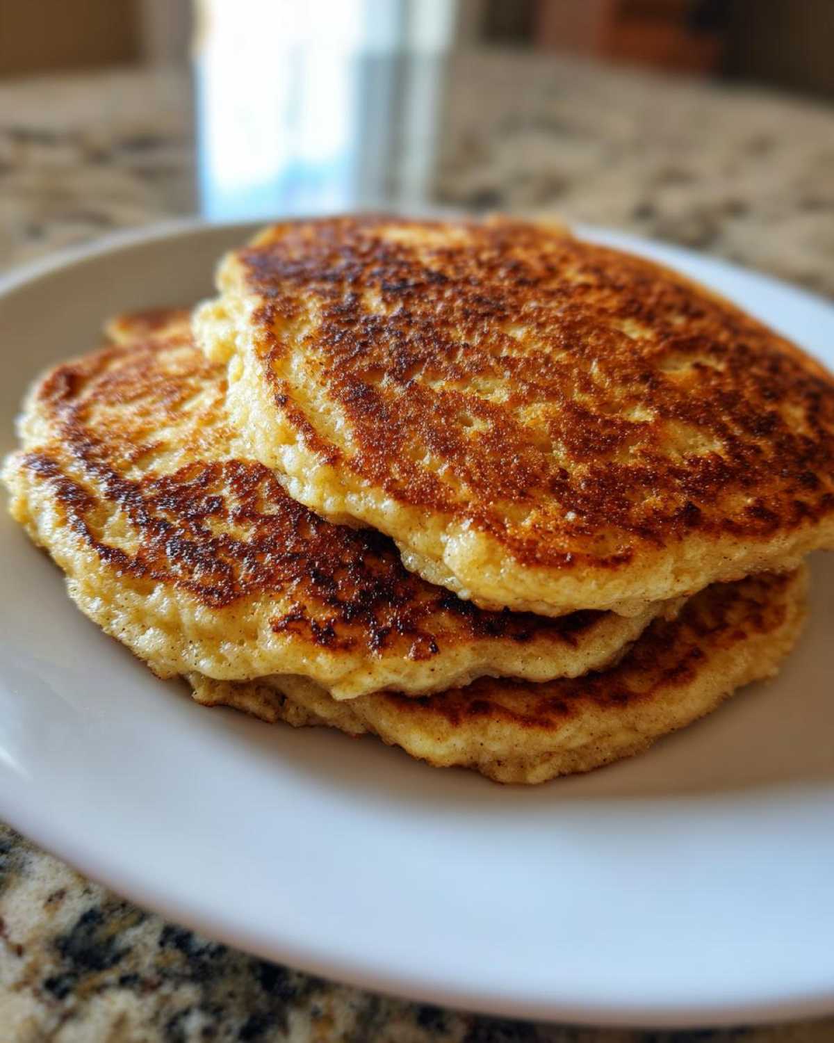 Close-up of a stack of three perfectly golden-brown Vegan Banana Oat Pancakes on a white plate.